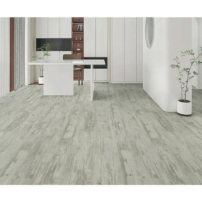 Suelo vinílico autoadhesivo Tren Grey - 152,4 x 914,4 x 2 mm, Gris - Interior de una habitación con suelo de madera gris claro, muebles blancos y plantas. El foco está en la estética del suelo.