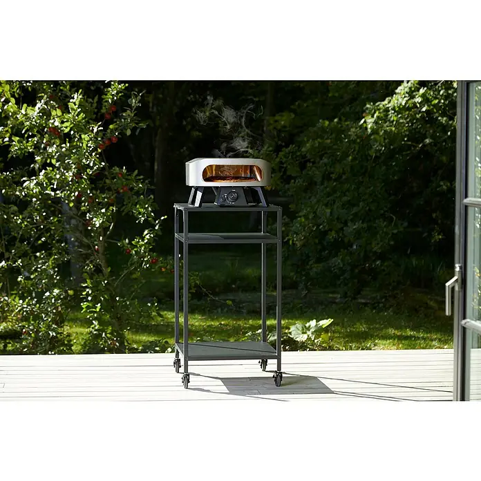 Cozze Pizzaofen Classic 13 - Grillfläche (B x T): 34 x 34 cm, 6 kW - Ein Ooni Pizzaofen auf einem grauen Metallwagen im Freien, ideal für Gartenpartys und kulinarische Erlebnisse im Freien.