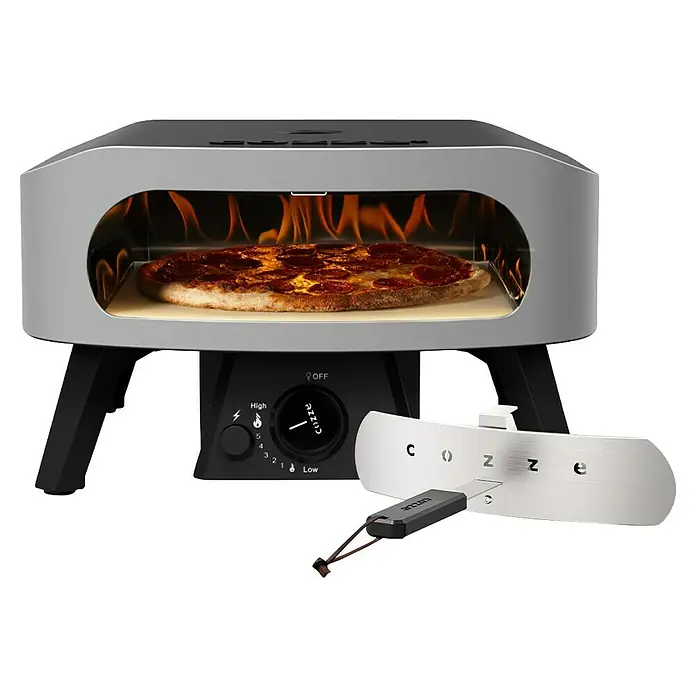 Cozze Pizzaofen Classic 13 - Grillfläche (B x T): 34 x 34 cm, 6 kW - Grauer und schwarzer tragbarer Pizzaofen mit backender Peperoni-Pizza und sichtbaren Flammen. Schwarzes Bedienfeld und Cozze Pizzaschneider dabei.