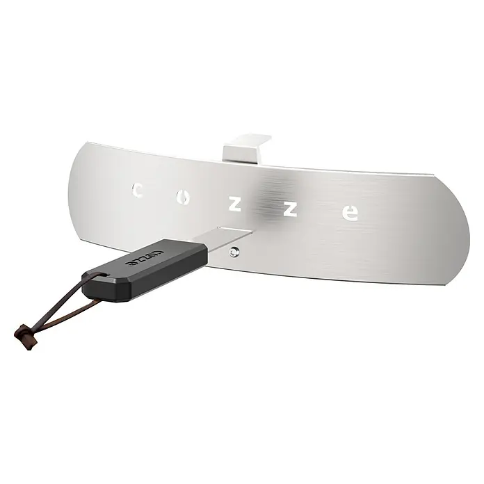 Cozze Pizzaofen Classic 13 - Grillfläche (B x T): 34 x 34 cm, 6 kW - Gebürstete silberne COZZE-Metallplatte mit ausgeschnittenen Buchstaben und einem daran befestigten dunkelgrauen COZZE-Gerät an einem braunen Lederriemen.