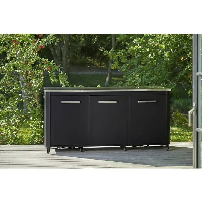 Cozze Outdoorküchen-Modul - Schwarz, B x T x H: 180 x 60 x 90 cm - Schwarzer Outdoor-Küchenschrank mit drei Türen und silbernen Griffen unter einer Edelstahlplatte auf einer Holzterrasse.