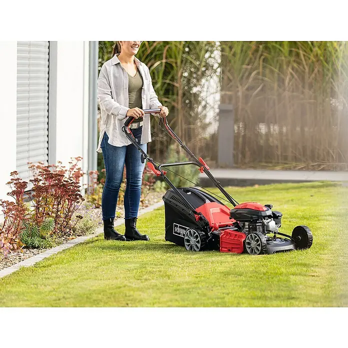 Scheppach Benzin-Rasenmäher PML46-161S - 150 cm³, Schnittbreite: 46 cm, Seilzugstarter - Eine Frau benutzt einen Scheppach Rasenmäher im Garten. Der Rasenmäher ist rot, schwarz und silber und hat einen Fangkorb.