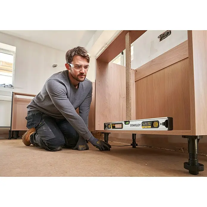 Stanley FatMax Nivel de burbuja Xtreme - Plateado - Un hombre usa un nivel Stanley para verificar si un gabinete base está nivelado. Ideal para trabajos de instalación precisos.