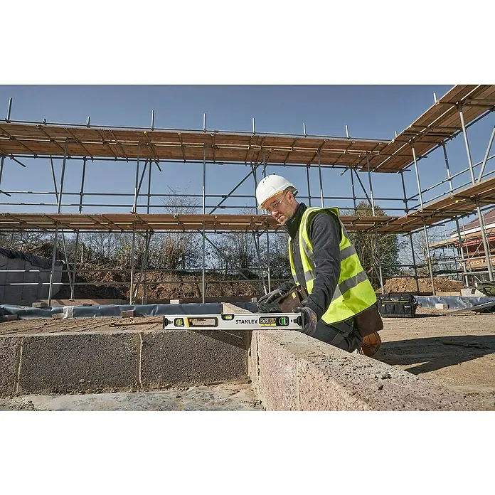 Stanley FatMax Nivel de burbuja Xtreme - Plateado - Un trabajador de la construcción con casco y chaleco de seguridad utiliza un nivel Stanley para nivelar una pared.