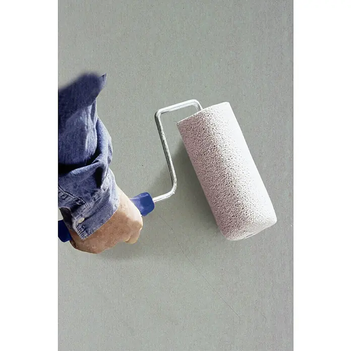 Knauf Betonkontakt - 20 kg - Eine Hand hält eine Farbwalze, die bereit ist, eine Wand zu streichen. Die Walze ist sauber und unbenutzt, bereit für die Renovierung.