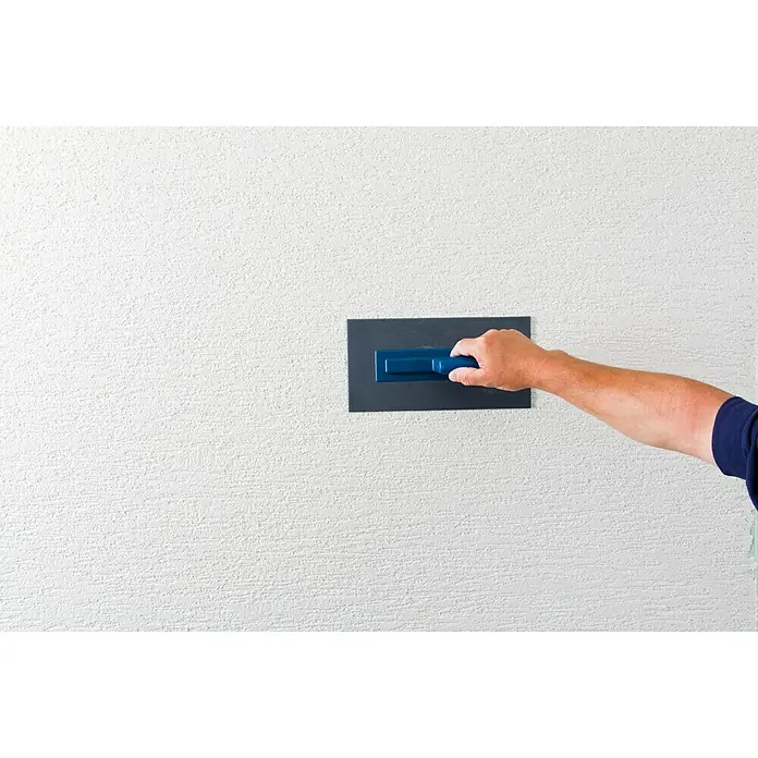 Knauf Dekoputz Royal-Fertigputz - Schneeweiß, Körnung: 2 mm, 20 kg, Konservierungsmittelfrei - Handwerker glättet eine weiße, strukturierte Wand mit einer grauen Glättkelle mit blauem Griff, um eine glatte Oberfläche zu erzielen.