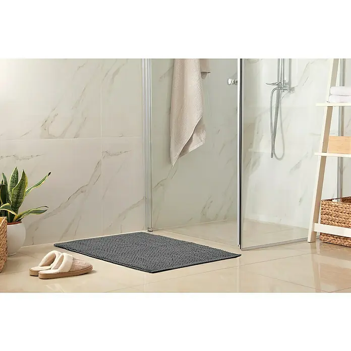 Badteppich Atlanta - 50 x 80 cm, Anthrazit, 100% Baumwolle - Ein grauer Badteppich liegt vor einer Dusche mit Handtuch und Pantoffeln im Badezimmer, neben einer grünen Pflanze im Topf.