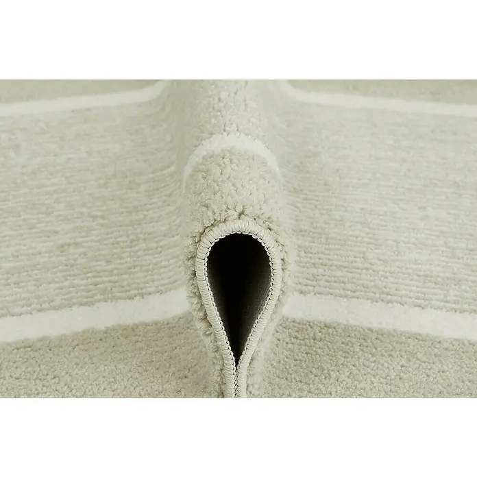 Badteppich Maui - 50 x 80 cm, Beige, 100% Polyester - Detailansicht eines beigen Teppichs mit Streifenmuster, gerollt, um die Textur und Verarbeitung hervorzuheben.