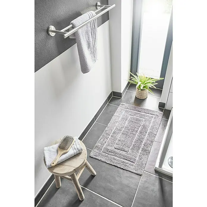 Badteppich Havanna - 50 x 80 cm, Taupe, Border, 80% Baumwolle, 20% Polyester - Ein Badezimmer mit einem grauen Teppich, einem Handtuchhalter mit Handtüchern, einem Hocker mit einer Bürste und einer Zimmerpflanze.