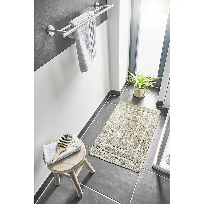 Badteppich Havanna - 50 x 80 cm, Beige, Border, 80% Baumwolle, 20% Polyester - Badezimmeransicht mit beigem Badteppich, Hocker mit Handtuch und Haarbürste sowie Handtuchhalter an grau-weißer Wand.