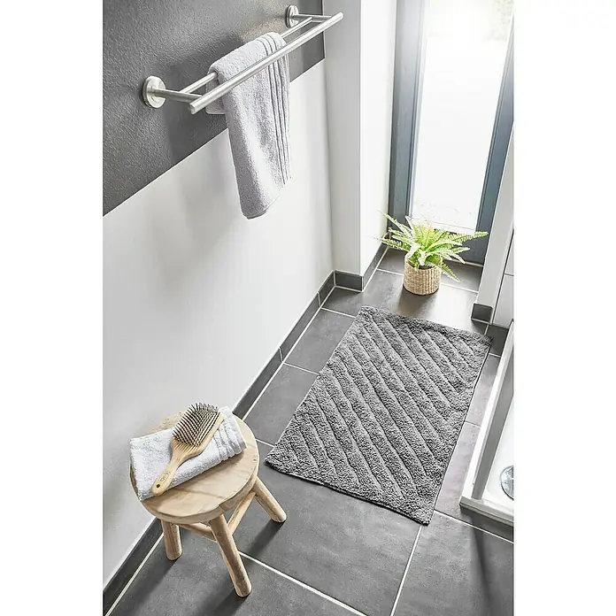 Badteppich Havanna - 50 x 80 cm, Grau, Stripe, 80% Baumwolle, 20% Polyester - Das Badezimmer zeigt eine graue Badematte mit diagonalem Muster auf dunklen Fliesen, neben einem Hocker mit Handtuch und Bürste.