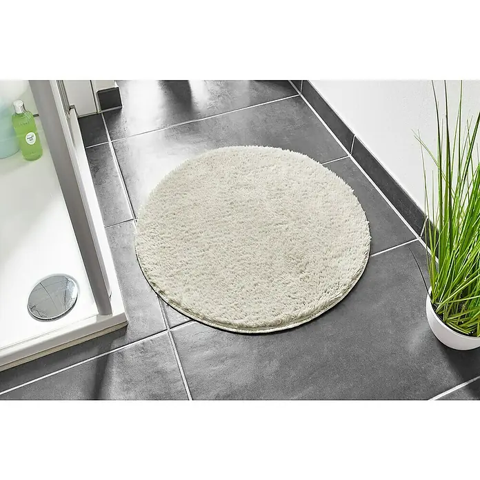 Badteppich Florida - 60 x 60 cm, Beige, 100% Polyester - Runder, cremefarbener Badteppich aus weichem Flor auf dunklen Fliesen im Badezimmer. Für ein angenehmes Gefühl nach dem Duschen.