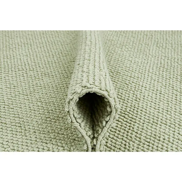 Badteppich Atlanta - 50 x 80 cm, Salbei, 100% Baumwolle - Nahaufnahme eines gerollten, hellgrünen Badezimmerteppichs mit gewebter Textur, der Komfort und Stil für jedes Badezimmer verspricht.