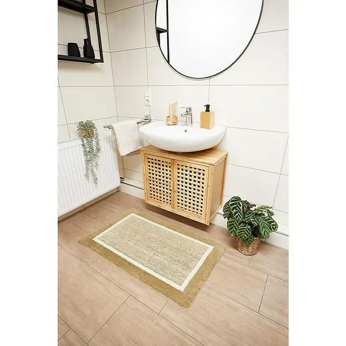 Badteppich Maui - 60 x 100 cm, Taupe, 100% Polyester - Badezimmeransicht mit rechteckiger Badematte in Beige und Weiß, die vor einem Unterschrank mit Waschbecken auf dem Boden liegt.
