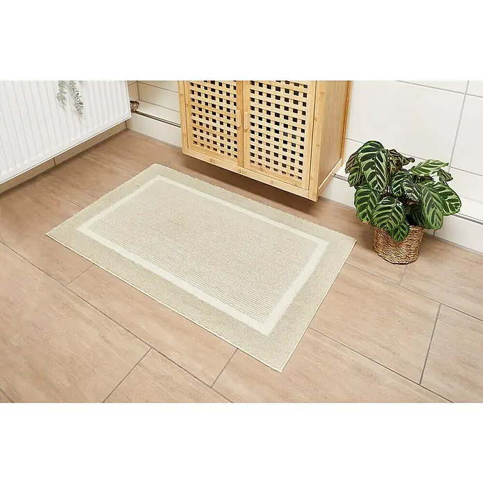 Badteppich Maui - 60 x 100 cm, Beige, 100% Polyester - Ein rechteckiger, beigefarbener Badteppich mit doppelter Bordüre liegt auf einem Badezimmerboden.
