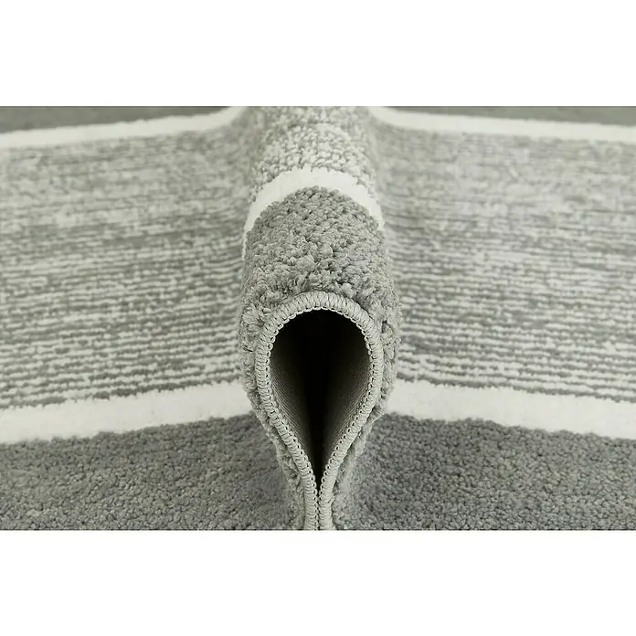 Badteppich Maui - 50 x 80 cm, Grau, 100% Polyester - Nahaufnahme eines gerollten, grau-weiß gestreiften Teppichs, der seine Textur und sein Design hervorhebt. Ideal für moderne Wohnräume.