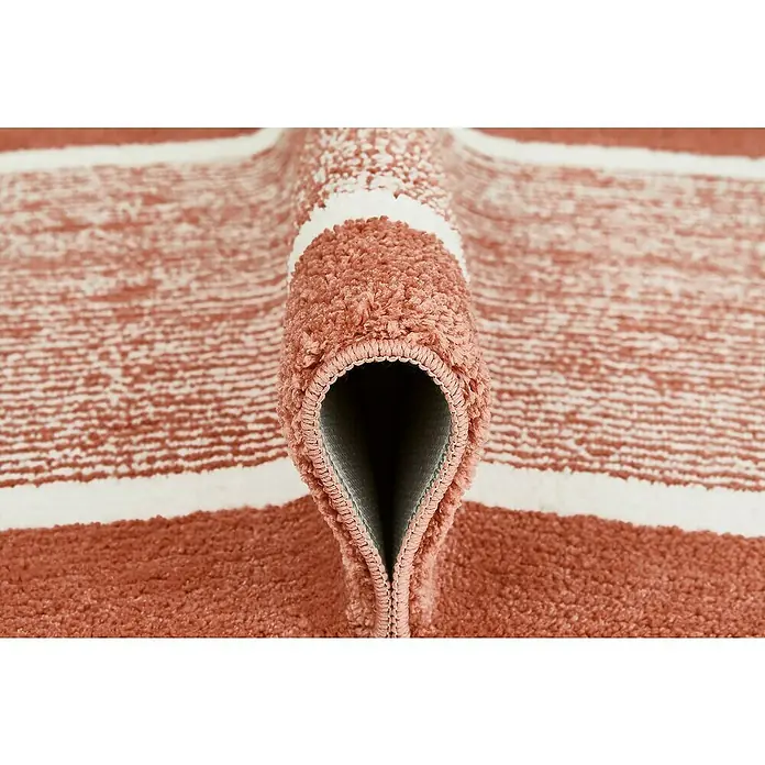 Badteppich Maui - 50 x 80 cm, Rostrot, 100% Polyester - Nahaufnahme eines korallenroten Teppichs mit weißen Streifen, der aufgerollt ist und seine Textur und Verarbeitung zeigt.