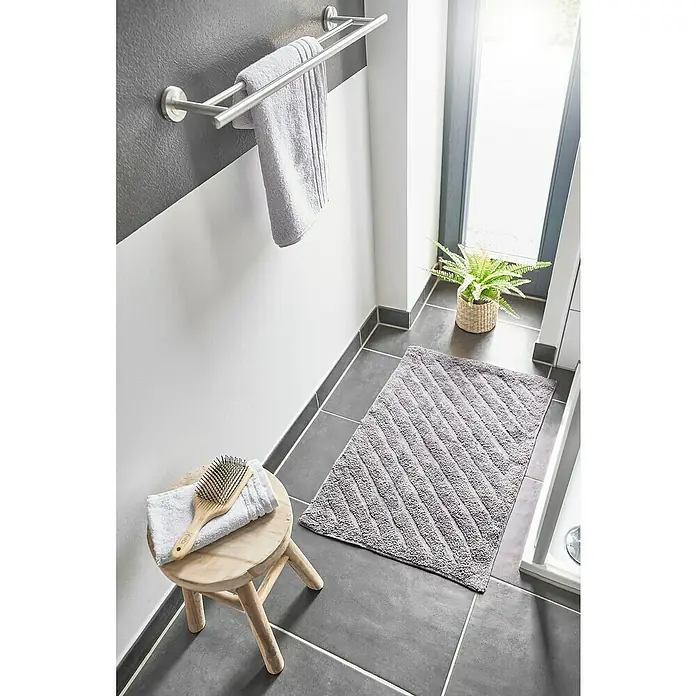 Badteppich Havanna - 50 x 80 cm, Taupe, Stripe, 80% Baumwolle, 20% Polyester - Ein Badezimmer mit grauem Teppich, Hocker mit Handtuch und Bürste, Handtuchhalter mit Handtuch, Pflanze und grauen Fliesen.