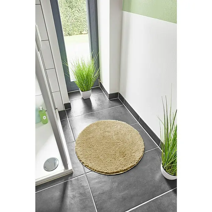 Badteppich Florida - 60 x 60 cm, Taupe, 100% Polyester - Ein runder, beiger Teppich liegt auf dunklen Fliesen im Badezimmer. Dekorative Pflanzen ergänzen das Badezimmerambiente.