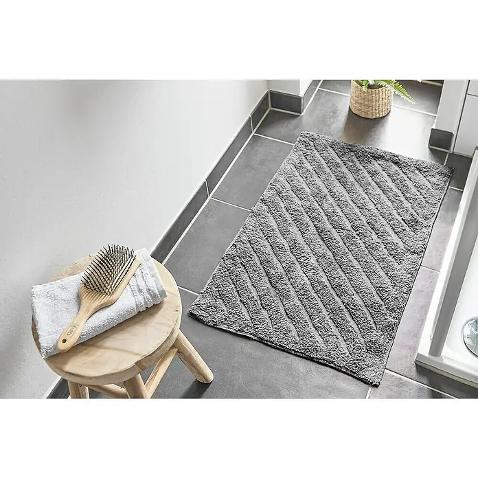 Badteppich Havanna - 50 x 80 cm, Grau, Stripe, 80% Baumwolle, 20% Polyester - Ein grauer Badteppich mit Streifenmuster liegt auf dunklen Fliesen neben einem kleinen Hocker mit einer Bürste und einem Handtuch.
