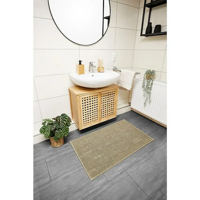 Badteppich Malibu - 60 x 100 cm, Taupe, 100% Polyester - Badezimmerteppich in Beige auf grauem Fliesenboden, passend zum Waschbeckenunterschrank aus hellem Holz.