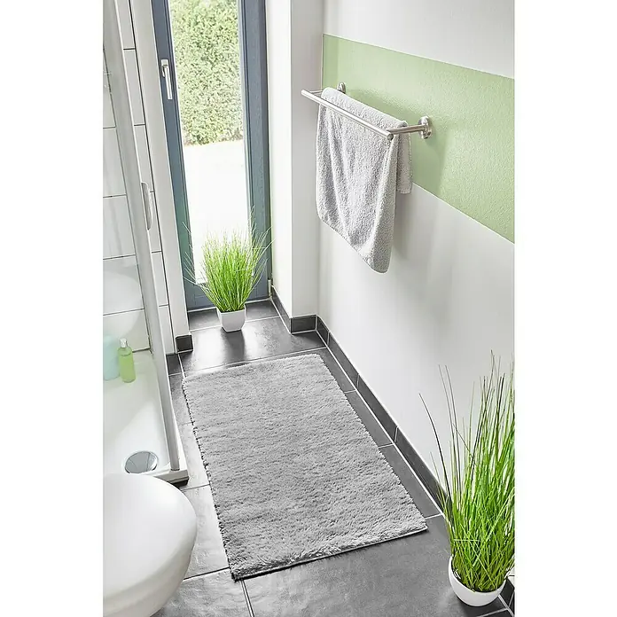 Badteppich Florida - 60 x 100 cm, Grau, 100% Polyester - Ein grauer Badteppich liegt auf dem grauen Fliesenboden vor dem Waschbecken, der Tür und einer grünen Wand mit Handtuchhalter.