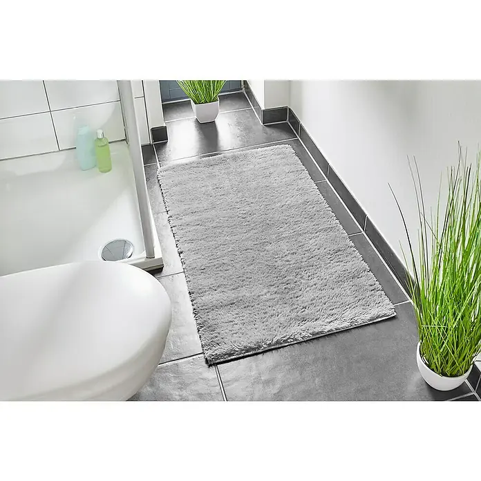 Badteppich Florida - 60 x 100 cm, Grau, 100% Polyester - Badezimmer mit weichem, grauem Teppich, Badewanne und Grünpflanzen. Der Teppich sorgt für Komfort und Stil im Raum.