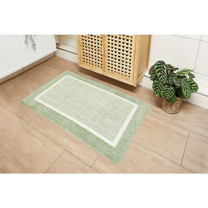 Badteppich Maui - 60 x 100 cm, Salbei, 100% Polyester - Ein rechteckiger, hellgrüner Badteppich mit weißem Innenrahmen liegt auf einem hellen Holzboden in einem Badezimmer.
