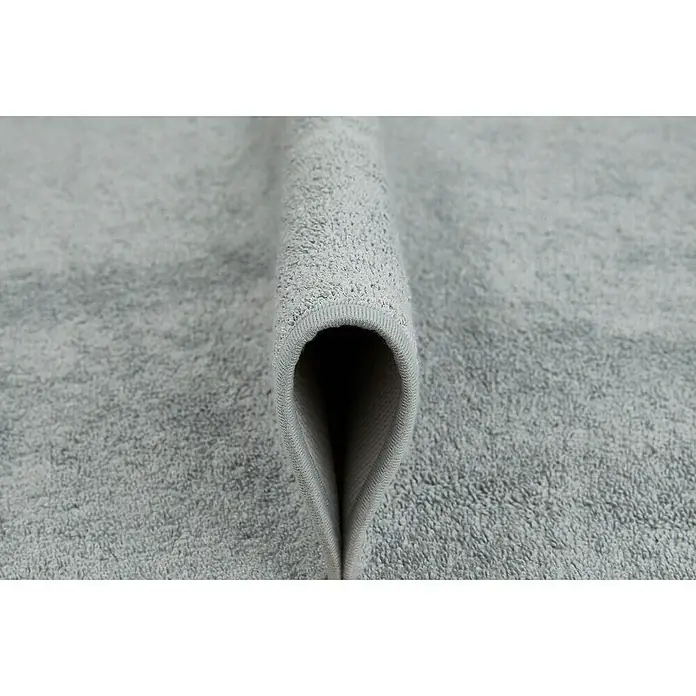 Badteppich Malibu - 60 x 100 cm, Grau, 100% Polyester - Nahaufnahme eines weichen, hellgrauen Handtuchs, das die Textur und die gewebte Kante hervorhebt. Ideal für Bad und Wellness.
