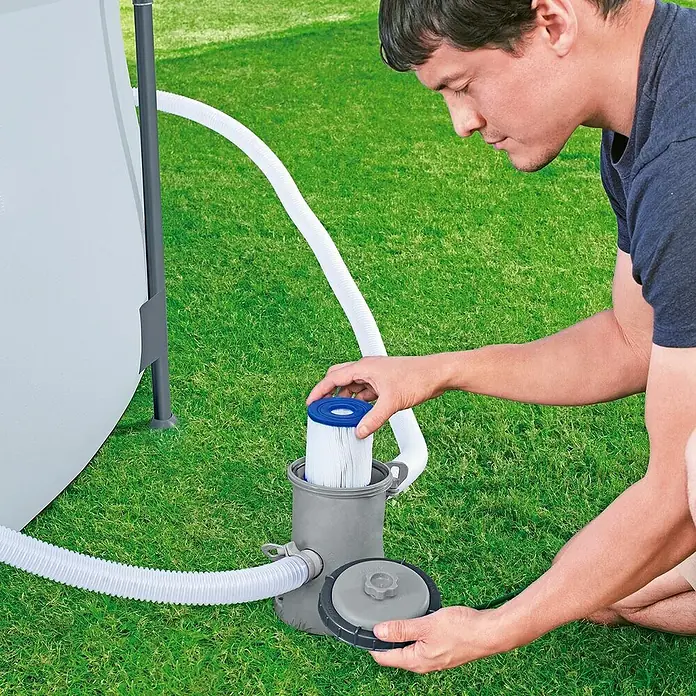 Bestway Filterkartusche - Filterleistung: 1.029 l/h - Mann, der eine Poolfilterkartusche in eine graue Poolfilterpumpe einsetzt, angeschlossen an einen Pool mit weißen Schläuchen auf grünem Gras.