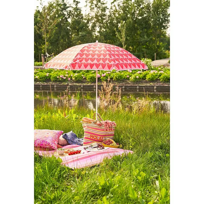 Mica Decorations Strandschirm - Rosa, Durchmesser Bespannung: 160 cm - Ein sonniger Tag am See mit einem pinkfarbenen Sonnenschirm mit Herzmuster, der eine Picknickdecke mit Köstlichkeiten beschattet.