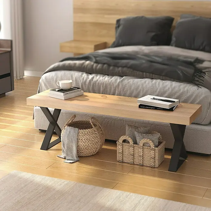 Rei Möbelfuß - B x H: 40 x 40 cm, Traglast: 200 kg, Stahl, Schwarz - Ein heller Holzschemel mit schwarzen X-förmigen Beinen vor einem Bett mit grauer Bettwäsche, dekoriert mit Büchern und Körben.