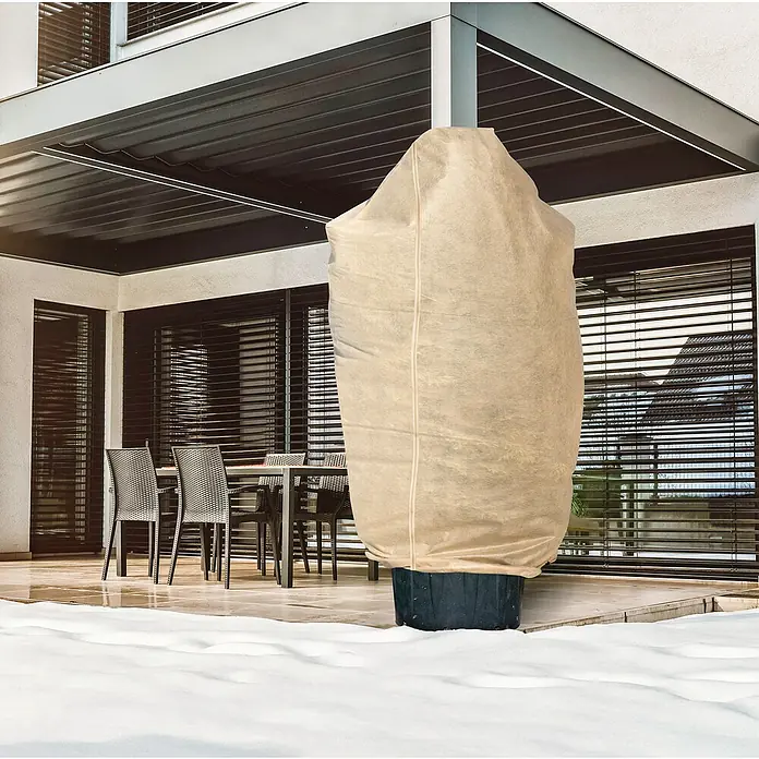 Windhager Winterschutzvlies Superprotect - L x B: 2,4 x 2 m, Beige, 100 g/m² - Ein Winterschutzsack für Pflanzen steht auf einer Terrasse im Schnee. Der Sack ist hellbraun und schützt die Pflanze vor Kälte.