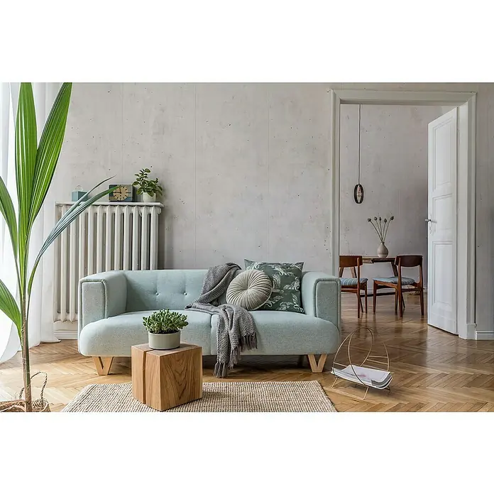 Grosfillex Wandpaneel Element 3D - Beton New York Weiss, 2.600 x 375 x 8 mm - Ein hellblaues Sofa mit dekorativen Kissen und einer Decke in einem stilvollen Wohnzimmer mit Holzboden und Zimmerpflanze.