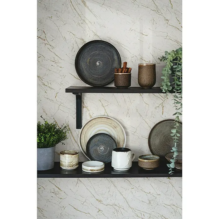 Grosfillex Wandpaneel Element 3D - Marble Calacatta, 2.600 x 375 x 8 mm - Ein Arrangement aus Keramikgeschirr und Dekorationsgegenständen auf zwei dunklen Regalen vor einem marmorierten Hintergrund.