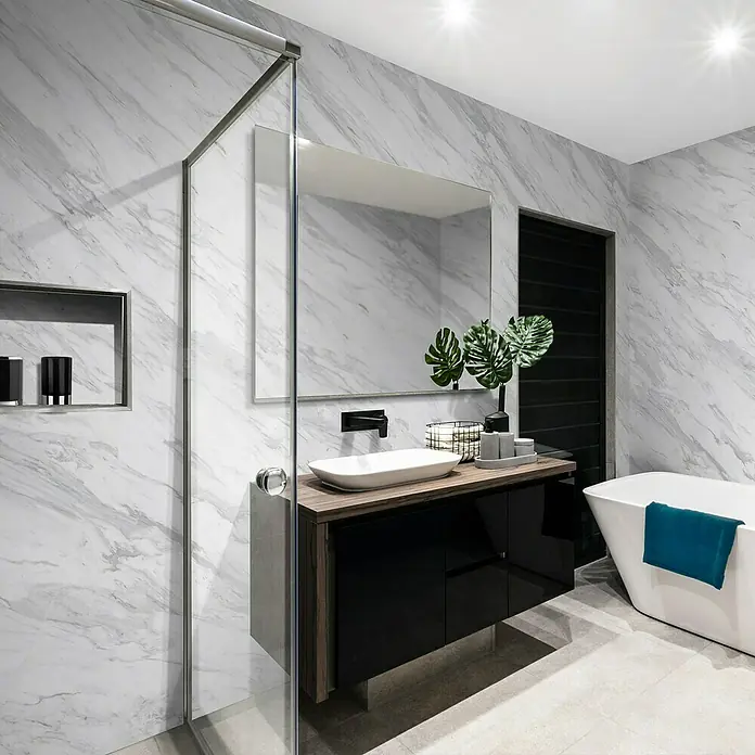 Grosfillex Wandpaneel Element 3D - Marbre Volakas, 2.600 x 375 x 8 mm - Elegantes Badezimmer mit Marmorwänden, einem modernen Waschtisch mit schwarzem Unterschrank und einer freistehenden Badewanne mit blauem Handtuch.