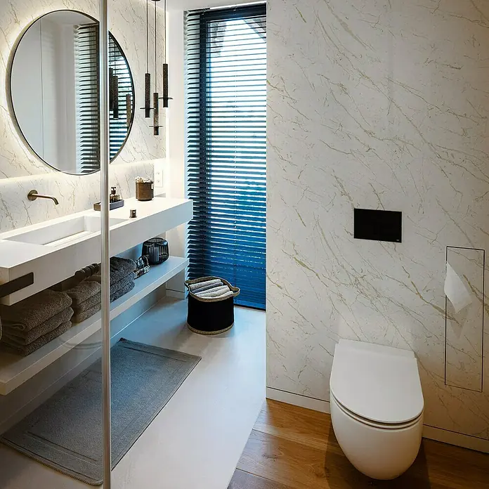 Grosfillex Wandpaneel Element 3D - Marble Calacatta, 2.600 x 375 x 8 mm - Elegantes Badezimmer mit einer modernen, wandhängenden Toilette. Marmorwände und Holzboden schaffen eine stilvolle Atmosphäre.