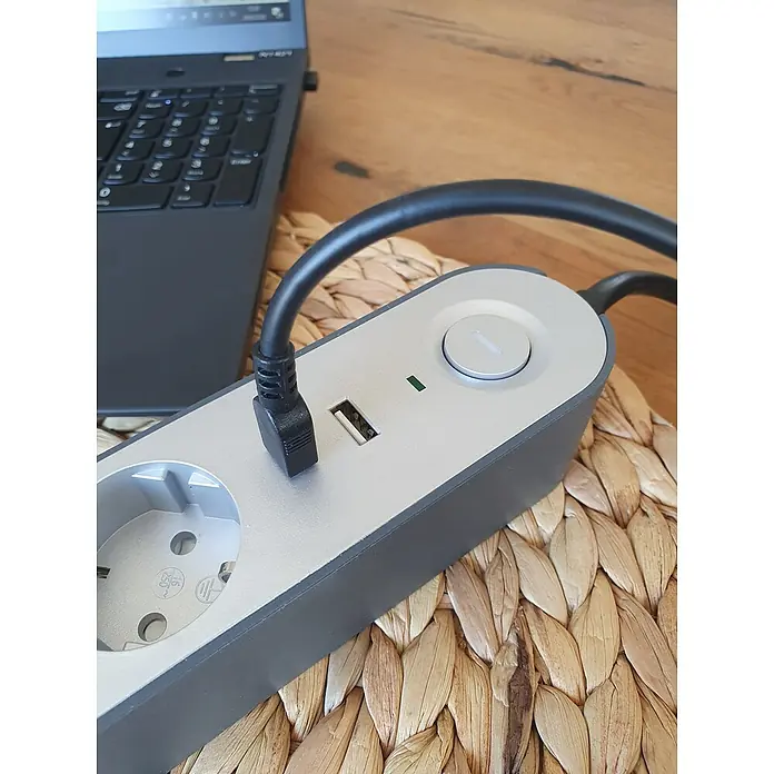 UniTEC Steckdosenleiste Greenline USB - Anzahl Steckdosen Schuko: 4 Stk., Silber, Anthrazit, Kabellänge: 1,8 m, Mit Schalter - Nahaufnahme einer Steckerleiste mit USB-Anschluss auf einem Tisch, neben einem Laptop, der Komfort und Konnektivität vereint.