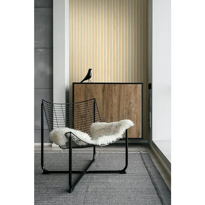 Grosfillex Wandpaneel Element 3D - Linio Bright Ash, 2.600 x 375 x 8 mm - Stilvolle Innenaufnahme mit einem modernen schwarzen Drahtsessel, einem weichen Fellkissen und einer Holzkommode mit Vogeldekoration.