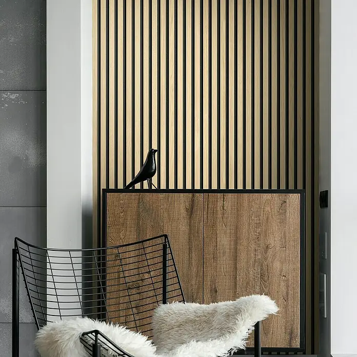 Grosfillex Wandpaneel Element 3D - Linio Ash, 2.600 x 375 x 8 mm - Moderne Inneneinrichtung mit einer Akzentwand aus Holzlatten, einem Holzschrank und einem stilvollen Drahtsessel mit weichem Kissen.
