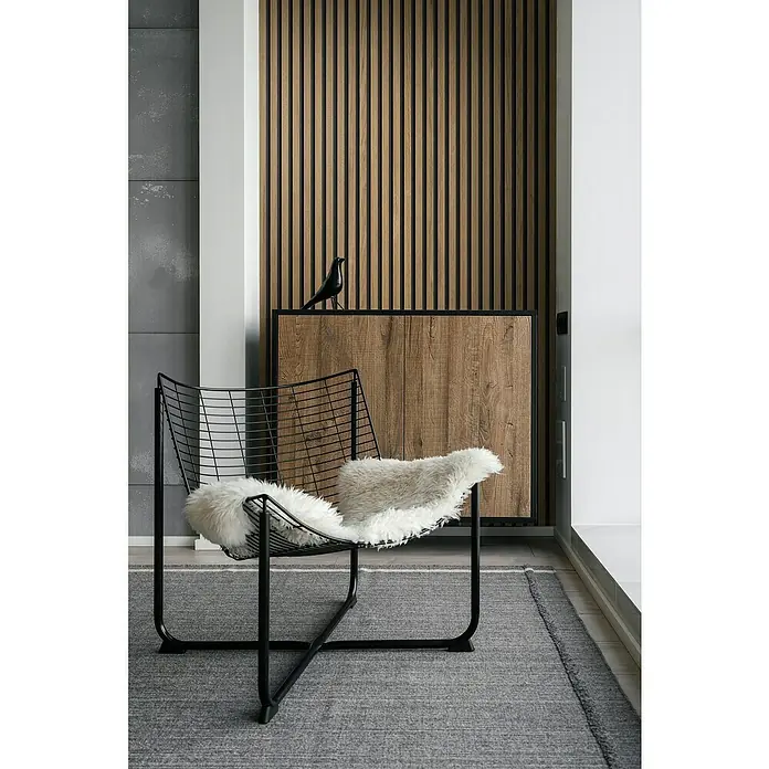Grosfillex Wandpaneel Element 3D - Linio Light, 2.600 x 375 x 8 mm - Stilvoller Innenraum mit einem modernen Drahtsessel mit flauschigem Kissen, der auf einem grauen Teppich vor einer Holzvertäfelung steht.
