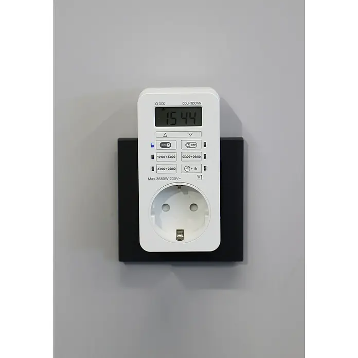 UniTEC Tages-Zeitschaltuhr Greenline Digital - Weiß, 3.680 W - Eine Zeitschaltuhr mit digitalem Display steckt in einer schwarzen Steckdose an einer grauen Wand.