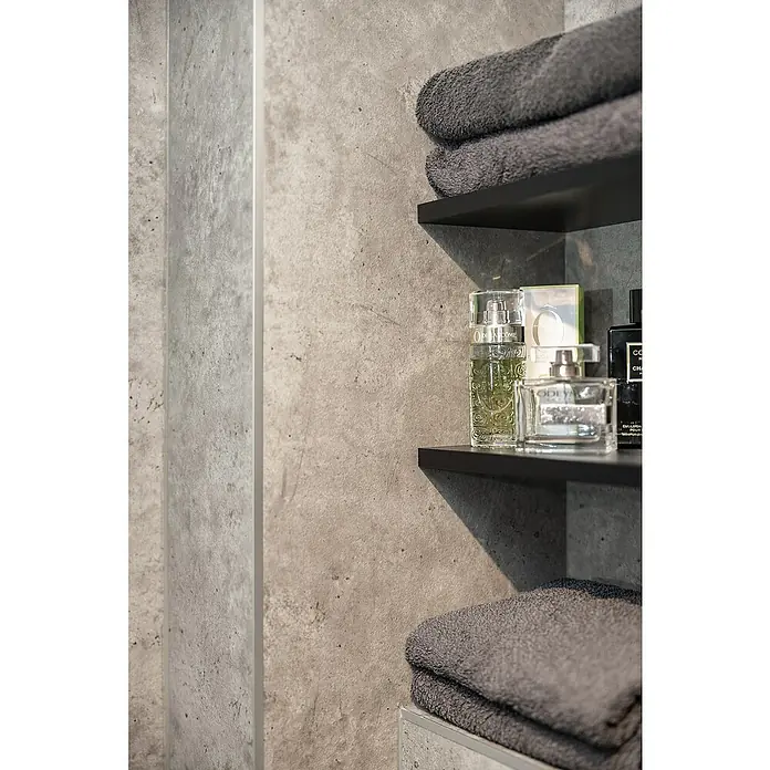 Grosfillex Wall+ Wandpaneel - Grey Concrete, 2.600 x 600 x 5 mm - Nahaufnahme von grauen Handtüchern und stilvollen Parfüms auf dunklen Regalen vor einer modernen, strukturierten Wand.