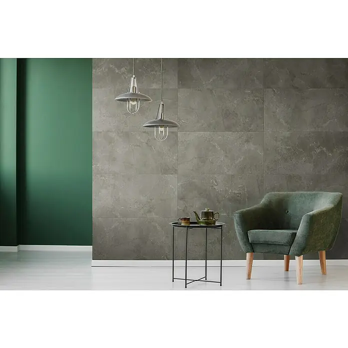 Grosfillex Wall+ Wandpaneel - Grey Marble, 600 x 300 x 5 mm - Graue Fliesenwand mit stilvoller Beleuchtung, die eine moderne und elegante Atmosphäre schafft. Ein grüner Sessel und Teewagen ergänzen das Design.
