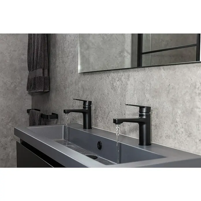 Grosfillex Wall+ Wandpaneel - Grey Concrete, 2.600 x 600 x 5 mm - Modernes Badezimmerwaschbecken mit zwei schwarzen Armaturen, aus denen Wasser fließt, vor einer grauen Betonwand und einem Spiegel.