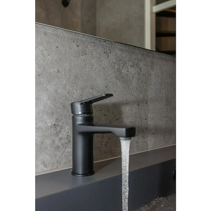 Grosfillex Wall+ Wandpaneel - Grey Concrete, 2.600 x 600 x 5 mm - Nahaufnahme einer schwarzen Armatur mit fließendem Wasser in einem modernen Badezimmer. Der matte Farbton und das minimalistische Design fallen auf.