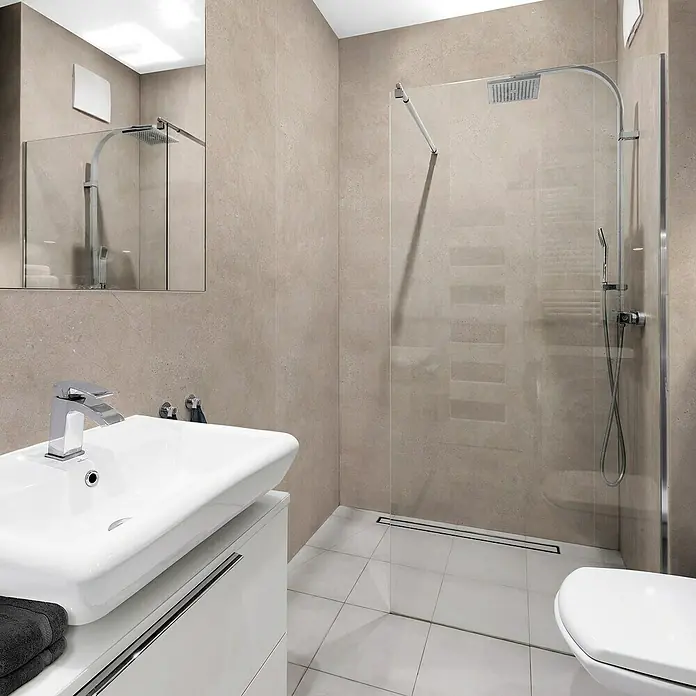 Grosfillex Wall+ Wandpaneel - Cream Slate, 2.600 x 600 x 5 mm - Ein modernes Badezimmer mit einem weißen Waschtisch und einer begehbaren Dusche, die durch eine Glaswand abgetrennt ist. Elegantes Design mit Fokus auf Funktionalität.