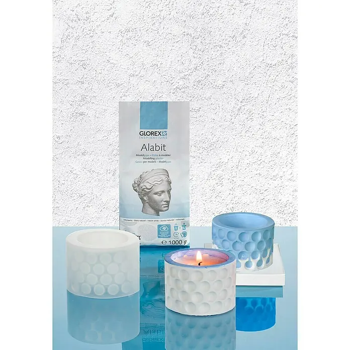 Glorex Modelliergips Alabit - 1 kg, Weiß - Ein 1000g Sack Glorex Alabit Modellgips steht neben selbstgemachten Teelichthaltern, einer davon mit brennender Kerze, auf einer blauen Oberfläche.