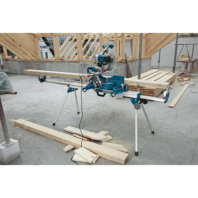 Bosch Professional Transport- & Arbeitstisch GTA 3800 - Arbeitshöhe: 824 mm, Traglast: 250 kg, Geeignet für: Kappsägen - Eine blaue Bosch Kapp- und Gehrungssäge mit Verlängerung auf einem Bauplatz, bereit für Holzarbeiten. Präzise Schnitte leicht gemacht.