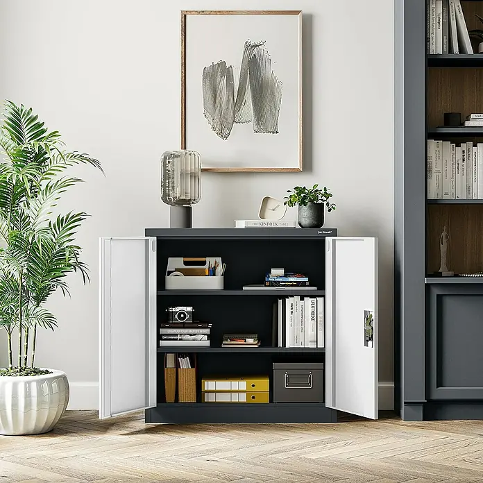 Jan Nowak Aktenschrank Beata - B x T x H: 90 x 40 x 92,5 cm, Anthrazit / Weiß - Ein grauer Büroschrank mit offenen, weißen Türen, gefüllt mit Bürobedarf, unter einem gerahmten Kunstwerk.